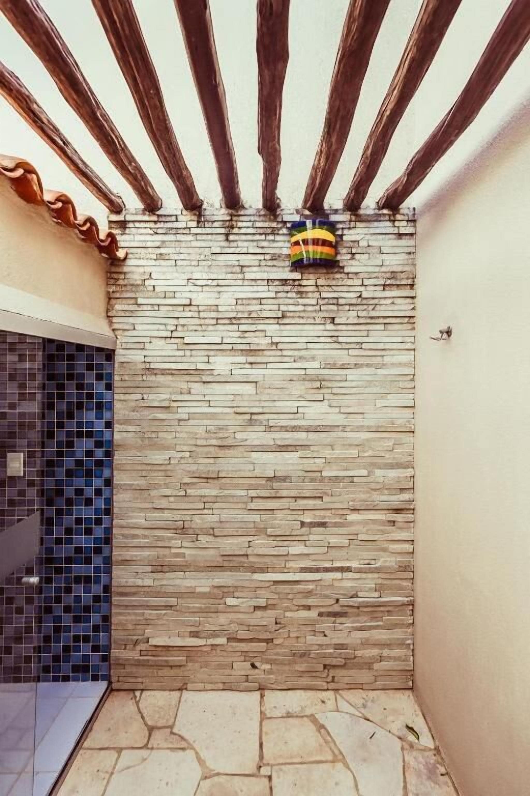 A small, enclosed outdoor area with a stone wall, wooden beams, and a tiled floor.