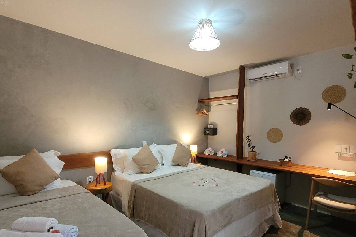 A hotel room with two beds, a desk, and a chair. There is a lamp on the desk and a wall-mounted air conditioner.