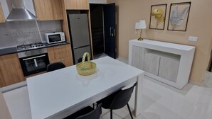 Een moderne keuken met een wit kookeiland, zwarte stoelen en een hanglamp.