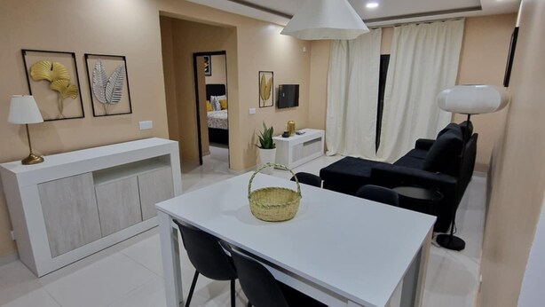 Een moderne woonkamer met een witte eettafel, zwarte stoelen, een witte bank en een televisie op een witte dressoir.