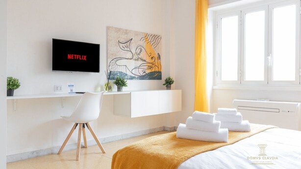 A modern hotel room with a flat-screen TV, a desk, a chair, a bed with towels, a window, and a painting on the wall. - Domvs Clavdia - Metro Station, 8 min to center, A-C (Roma)