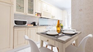 A modern kitchen with white cabinets, a microwave, and a dining table set for two. - Domvs Clavdia - Metro Station, 8 min to center, A-C (Roma)