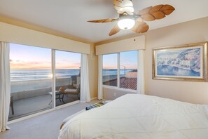 Un dormitorio con una cama grande, ventilador de techo y vista al océano a través de amplias ventanas.