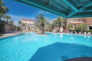 A swimming pool with lounge chairs and palm trees, surrounded by multi-story buildings with balconies. - New Heated Pool & Hot TUB!  Direct Pool Access (Galveston)