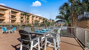 A balcony with a table set for dining, surrounded by chairs, overlooking a pool and a building with multiple balconies. - New Heated Pool & Hot TUB!  Direct Pool Access (Galveston)