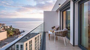 Un balcon avec vue sur la mer, des fauteuils en osier et une table sur laquelle se trouvent un chapeau et une boisson orange.