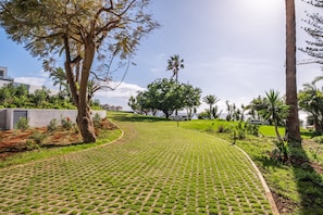 A paved pathway leading through a landscaped area with trees and a view of buildings in the background. - Ocean s Whisper by Homie (Funchal)