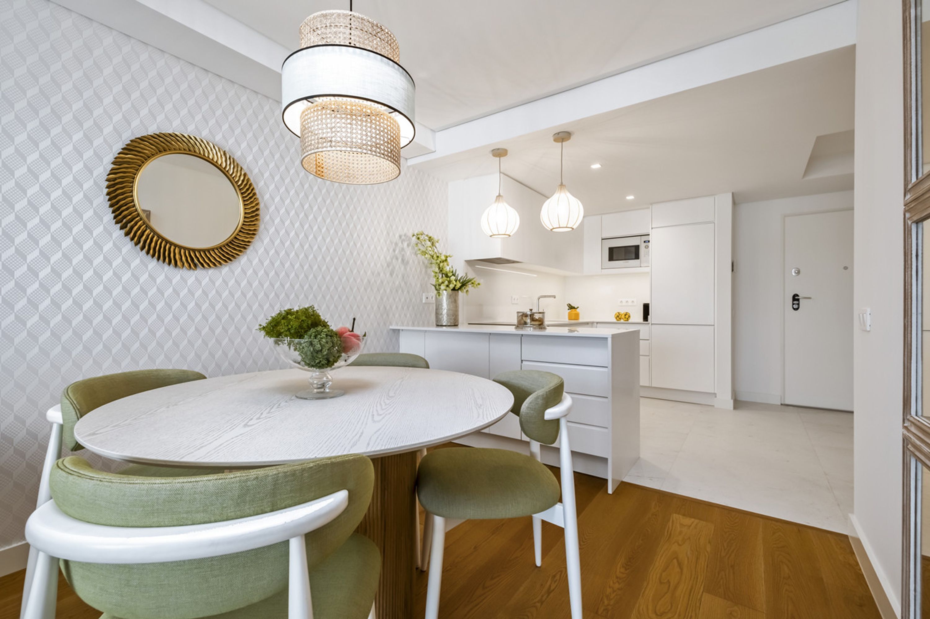 A modern kitchen with white cabinetry, a round dining table with green chairs, and pendant lighting.