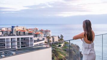 A woman standing on a balcony overlooking a coastal cityscape with buildings and the sea.