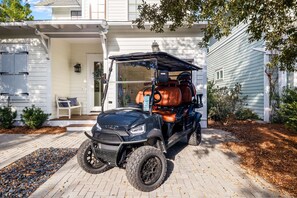 Une voiturette de golf est garée devant une maison dotée d’un porche, d’un petit jardin et d’un chemin menant à l’entrée.