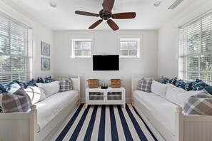 Une chambre avec deux lits blancs, un ventilateur de plafond, un téléviseur à écran plat et un tapis à rayures.