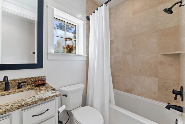 A bathroom with a granite countertop sink, a toilet, a shower with a black faucet, and a window with a view of trees. - New Specials! 6 Seater Cart, Bikes & Beach Toys, Gated Beach Community (SANTA ROSA BEACH)