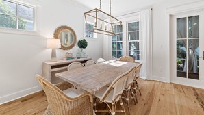 A dining area with a wooden table, wicker chairs, a hanging light fixture, and large windows with curtains. - New Specials! 6 Seater Cart, Bikes & Beach Toys, Gated Beach Community (SANTA ROSA BEACH)
