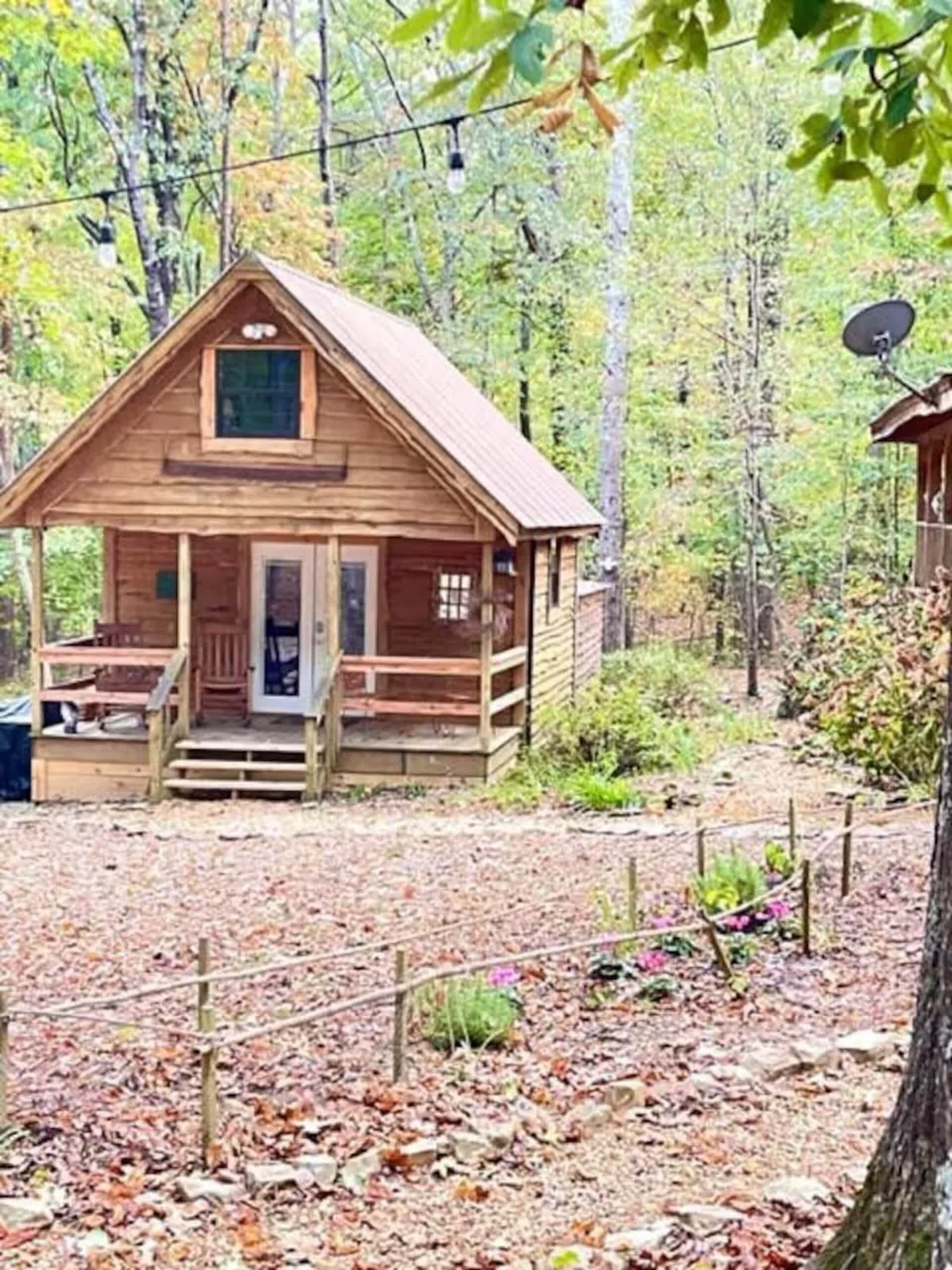 A wooden cabin with a porch, surrounded by a forest.