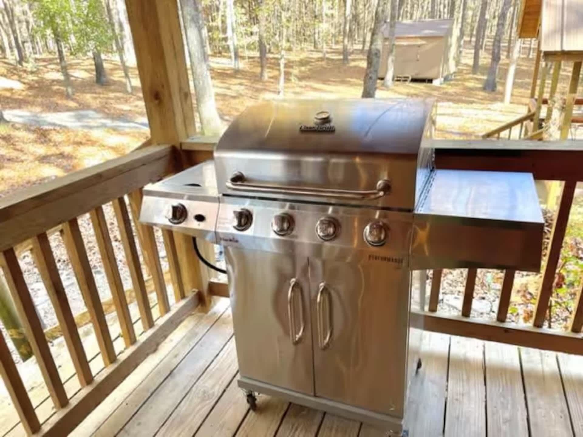 Un barbecue extérieur en acier inoxydable, installé sur une terrasse en bois, avec vue sur une zone boisée.