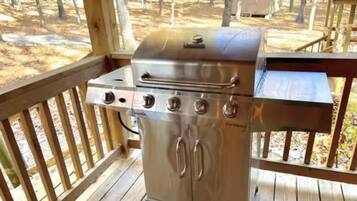 Un barbecue extérieur en acier inoxydable, installé sur une terrasse en bois, avec vue sur une zone boisée.