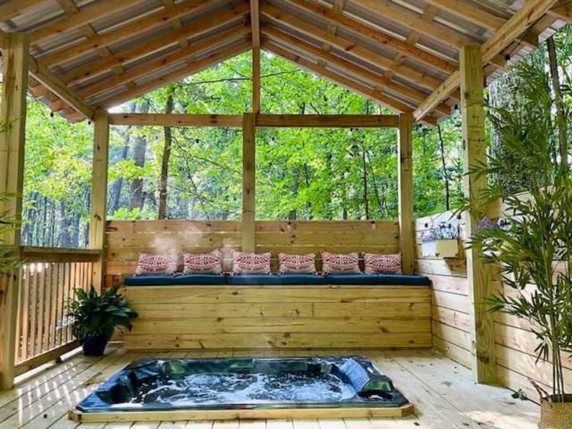 A wooden deck with a hot tub, wooden benches, and a view of a forest.
