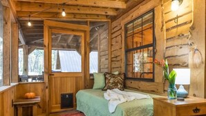 A cozy log cabin bedroom with a bed, a small table, a lamp, and a window. - Hot Tub, Fire Pit & Games! Family Falcon Lodge (Mentone)