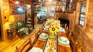 A wooden cabin interior with a dining table set for four, a chandelier, a painting on the wall, and a staircase. - Hot Tub, Fire Pit & Games! Family Falcon Lodge (Mentone)
