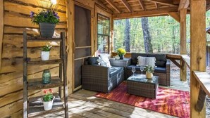 A cozy cabin interior with wicker furniture, a wooden ladder, and a view of the forest. - Hot Tub, Fire Pit & Games! Family Falcon Lodge (Mentone)