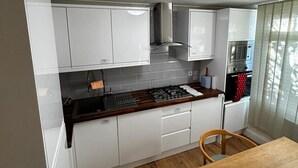 Una cocina compacta con armarios blancos, una encimera de madera, una estufa a gas, un microondas y una mesa de comedor con sillas.