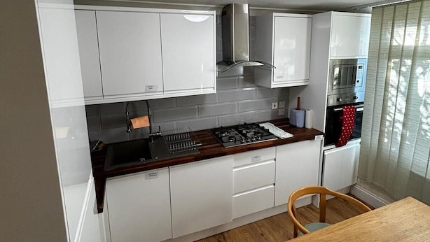 Una cocina compacta con armarios blancos, una encimera de madera, una estufa a gas, un microondas y una mesa de comedor con sillas.