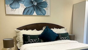 Una cama bien hecha con ropa blanca y dos almohadas, una de ellas con la palabra 'love'.