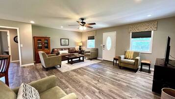 A spacious living room with a ceiling fan, a wooden cabinet, a television, and a dining area with a table and chairs.