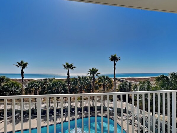 A pool area with a view of the beach and palm trees.