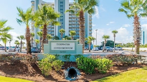 A sign for the Tidewater Condominium with a clear view of the building in the background. - Tidewater (Orange Beach) #108 | Gulf Front + Resort Amenities (Orange Beach)