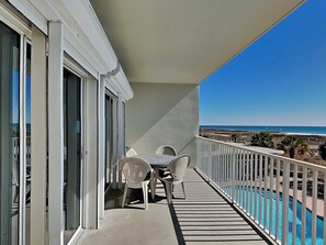 Een balkon met een tafel en stoelen, met uitzicht op een zwembad en een strand.