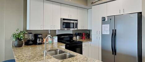 A modern kitchen with granite countertops, stainless steel appliances, and white cabinetry.