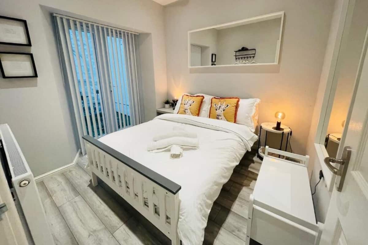 A modern bedroom with a large bed, bedside tables, a mirror, and a window with blinds.