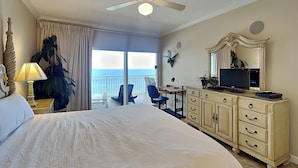 A hotel room with a large bed, a ceiling fan, a television, a desk, and a view of the ocean. - Admiral's Quarters #1406 | Gulf Front + Amenities (Orange Beach)