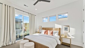 Une chambre moderne avec un grand lit, deux tables de chevet, un ventilateur de plafond et une vue sur le balcon.