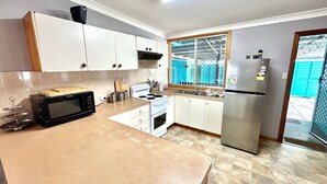 Una cocina con armarios blancos, un microondas negro, un refrigerador de acero inoxidable y una ventana con vista a un edificio azul.