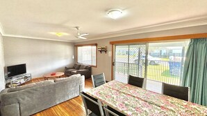 Una sala de estar con sofá, televisor, mesa con mantel floreado y balcón con vista.