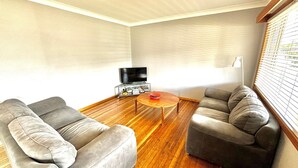 Una sala de estar con dos sofás grises, una mesa de centro y un mueble de televisión con libros y un control remoto.