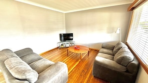 A living room with two grey sofas, a coffee table, and a TV stand with books and a remote. - Sunshine on Heath -Pet Friendly (Evans Head)