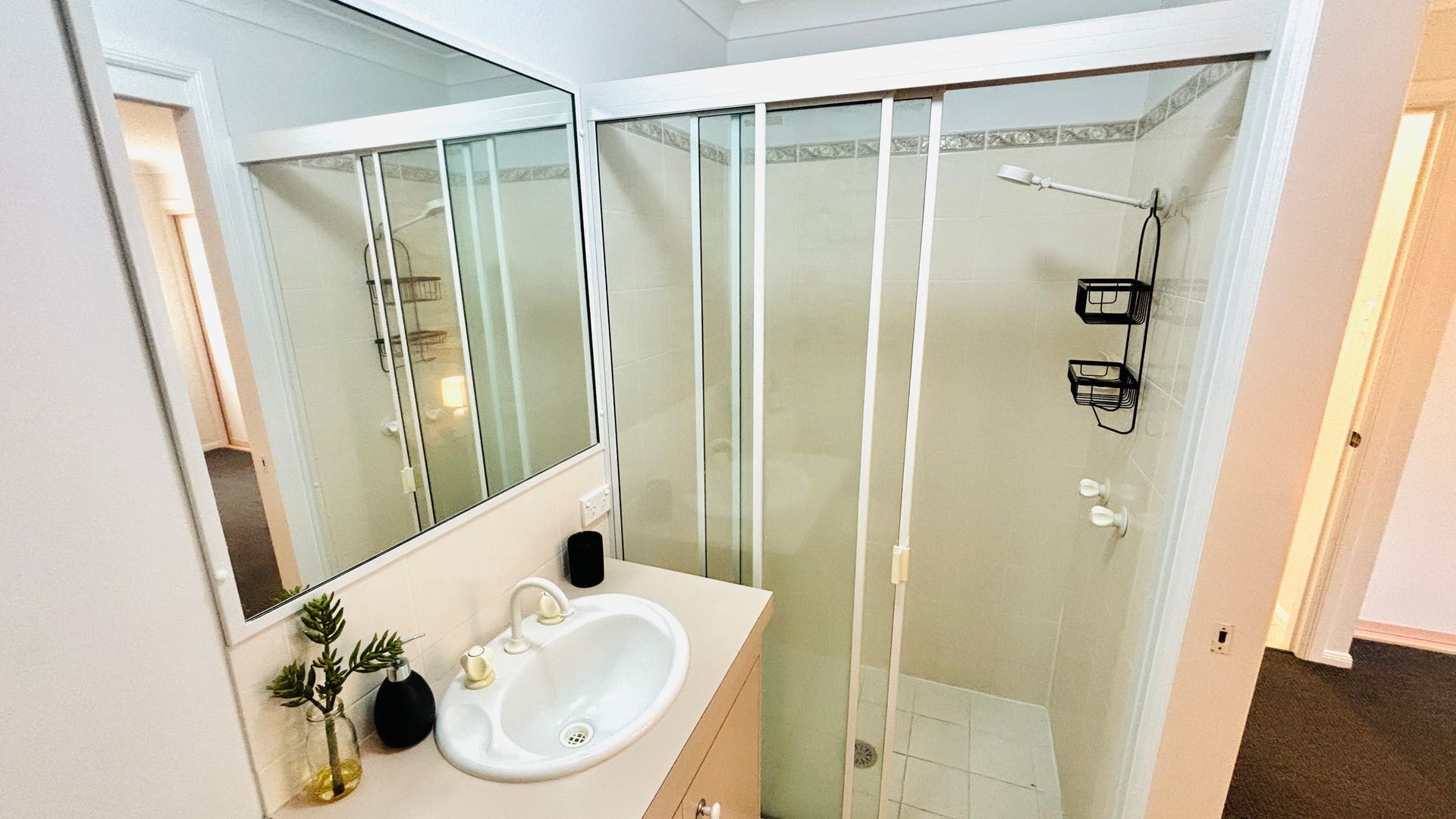 Ein Badezimmer mit einem weißen Waschbecken, Spiegel und einer Duschkabine aus Glas.