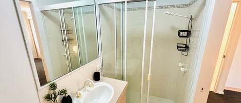 Ein Badezimmer mit einem weißen Waschbecken, Spiegel und einer Duschkabine aus Glas.