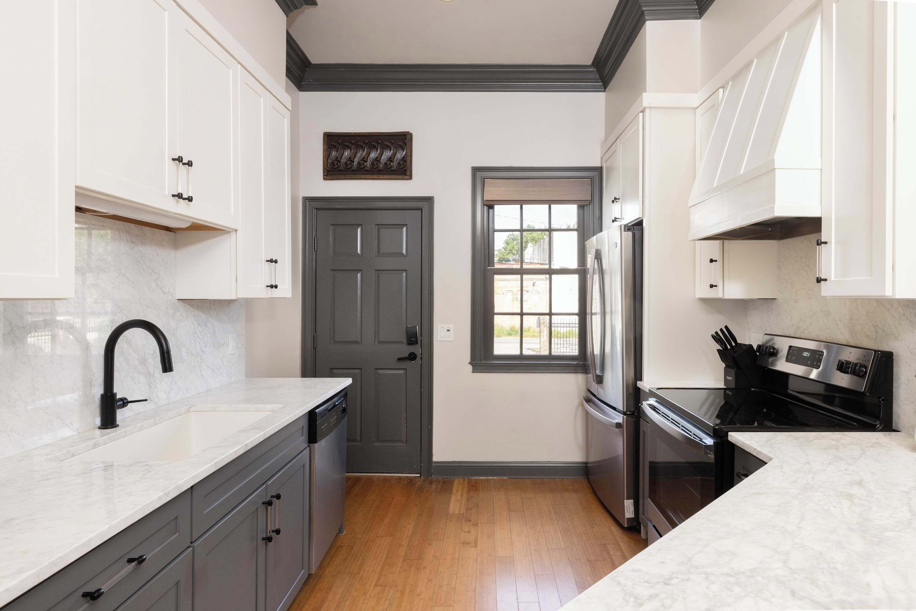 A kitchen with white cabinets, a gray door, a window, and stainless steel appliances.
