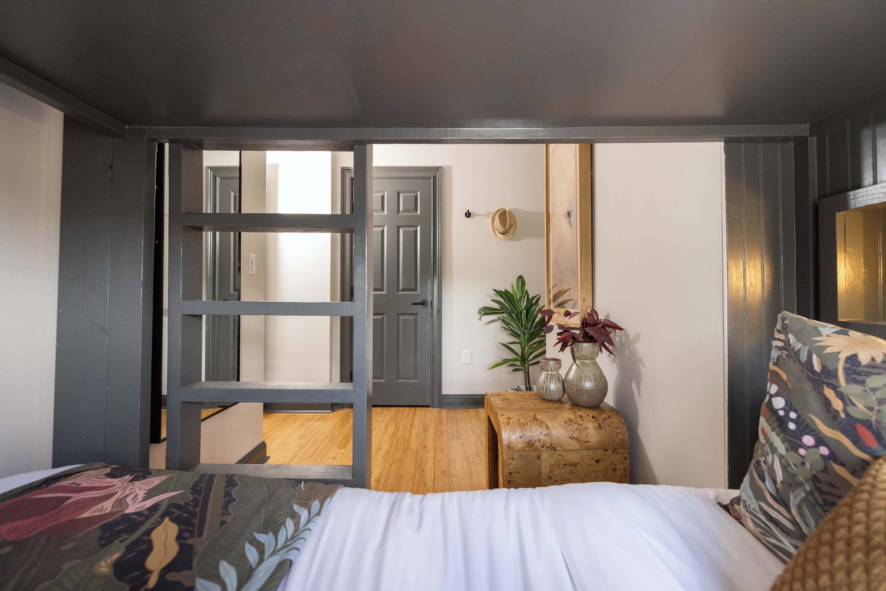 Een slaapkamer met een bed, een nachtkastje, een plant en een deur naar een andere kamer.