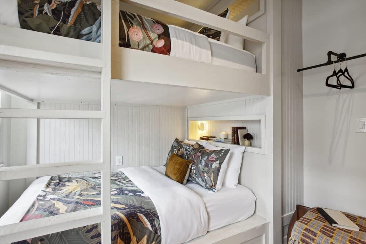 Une chambre avec un lit superposé aux couleurs claires, une petite table de chevet avec une lampe et un porte-manteau mural.