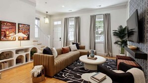 Un salon moderne avec un canapé d’angle, une table basse ronde et une grande fenêtre agrémentée de rideaux.