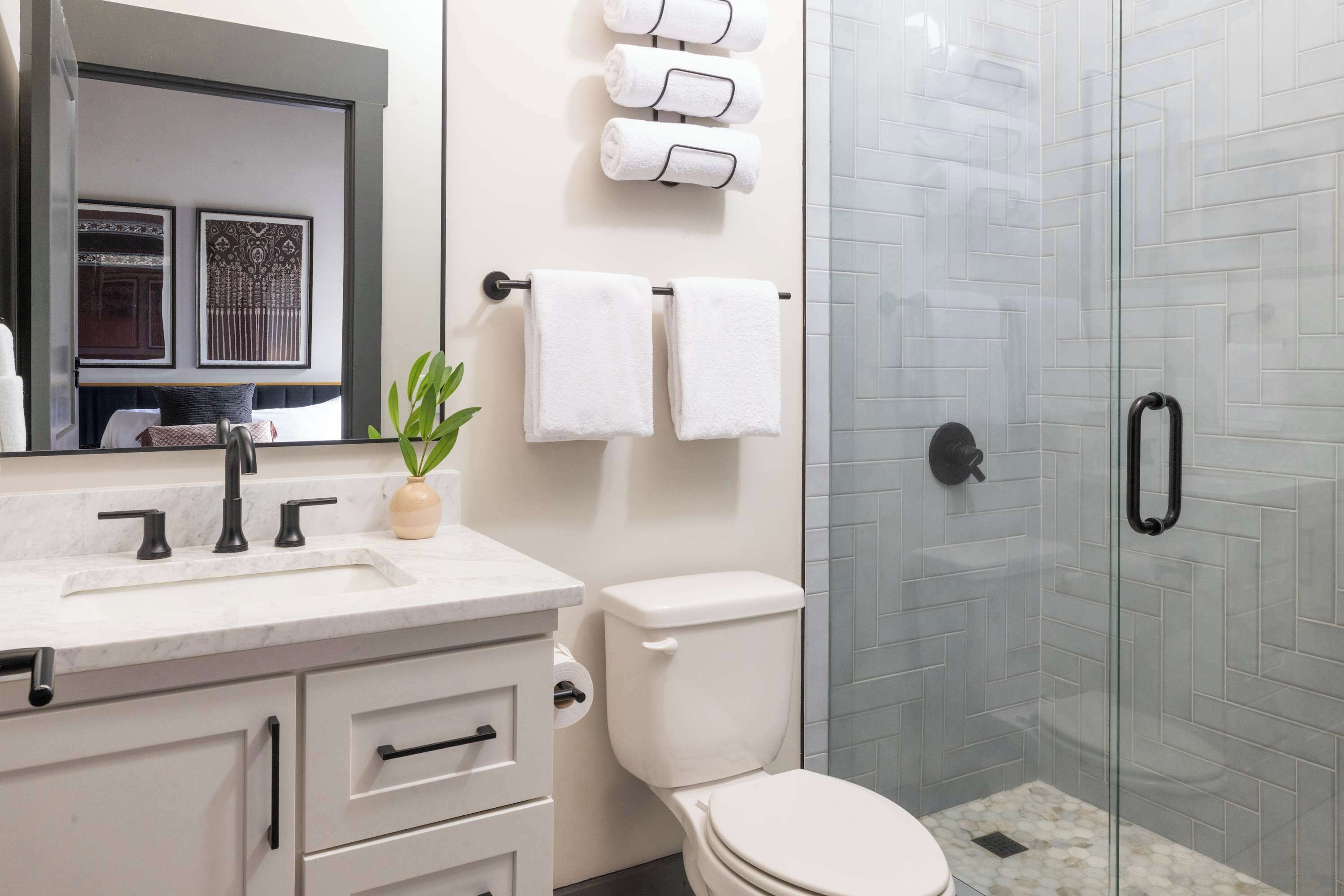 A modern bathroom with a white sink, black faucet, a toilet, and a glass shower enclosure.