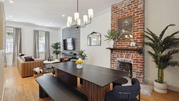 Un salon moderne avec une table à manger en bois foncé, un canapé et une cheminée avec un mur en briques.