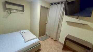 A small, clean room with a single bed, a TV mounted on the wall, and a door leading to another room.