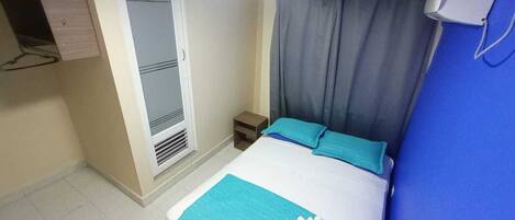 A hotel room with a bed, a small bedside table, a wardrobe, and a window with curtains.
