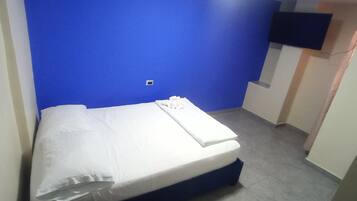 A room with a bed, a blue wall, and a flat-screen TV mounted on the wall.